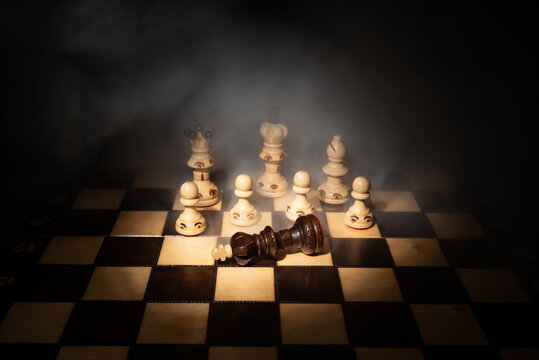 Dark chess king fallen on chessboard among white pieces in dramatic smoke. Concept of checkmate, defeat, business strategy, competition and leadership.