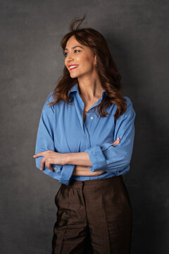 Smiling confident woman in blue shirt standing against dark studio background