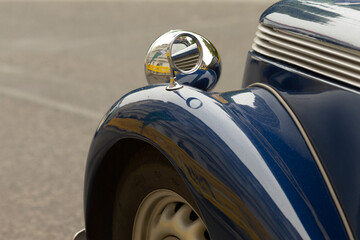 Fototapeta premium Detailed close-up of the front left fender and round headlight of a glossy blue vintage car. Visible features include chrome headlight housing, curved metal