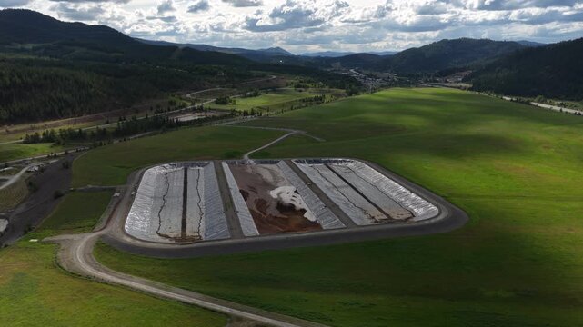 Aerial of waste water treatment tanks in Kellogg Idaho with green field under cloudy spring skies