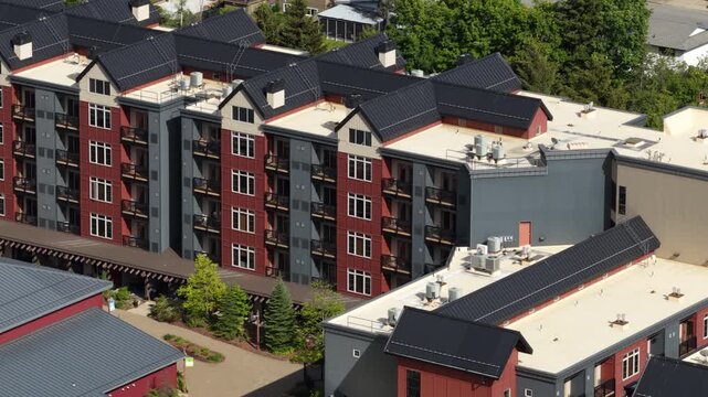 Aerial of residential buildings in Kellogg Idaho on sunny spring time showing multiple multistory apartment complexes with dark roofs