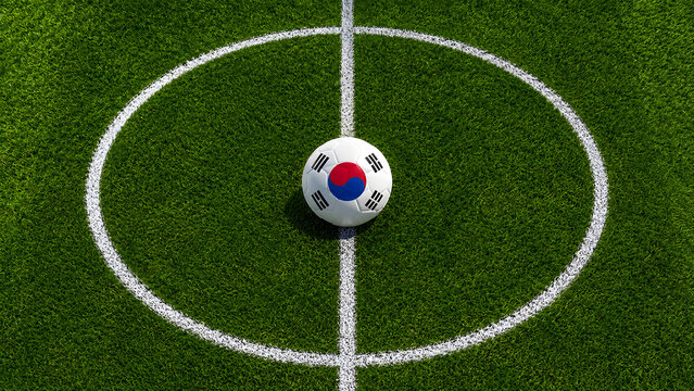 A high-angle shot of a soccer ball featuring the South Korean flag pattern, placed perfectly in the center circle of a vibrant green artificial grass pitch.
