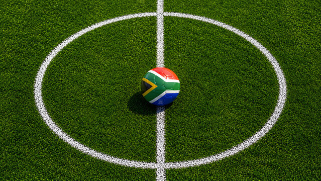A soccer ball featuring the South African flag pattern placed in the center of a white circle on a green artificial turf field, top-down view.