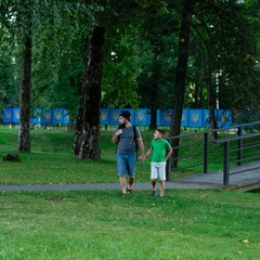 Fototapeta premium A father and son stroll through a park, enjoying a leisurely afternoon together.