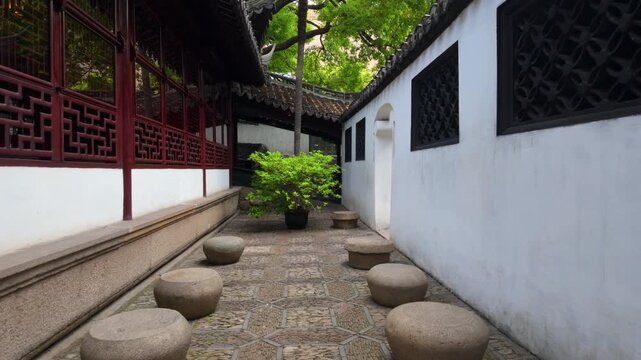 Stone stools line a tiled pathway beside white walls and a potted green shrub outdoors