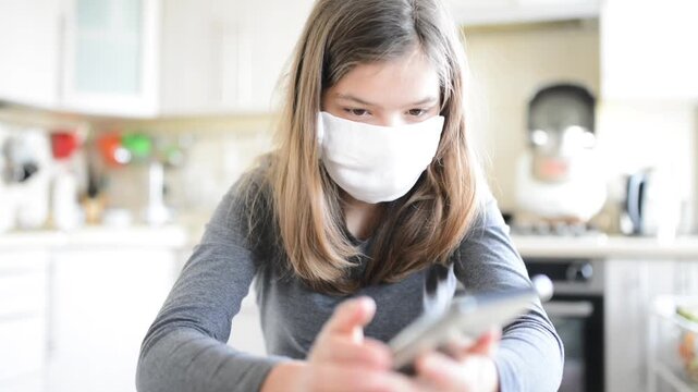 Young beautiful girl in medical mask sits at table and dials number on smartphone