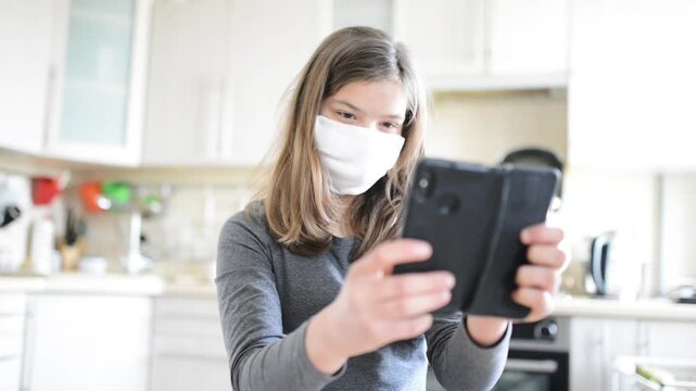 Young beautiful girl looks at black smartphone. In background, kitchen.