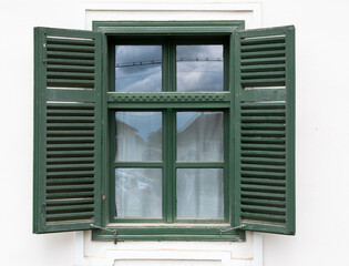 Fototapeta premium Close-up of vintage wooden window with green shutters on white exterior wall, rural architecture detail in Romania.