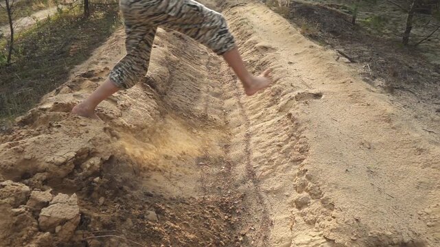 Girl in camouflage pants and pink T-shirt jumps through sandy moat. Slow motion. Evening time, sunset.