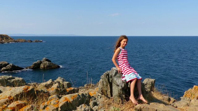 Little girl sitting on rocky shore of sea