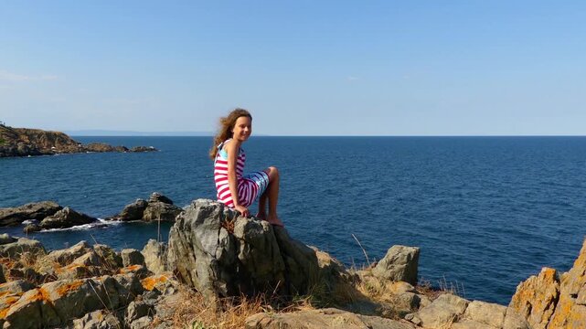 Little girl sitting on rocky shore of sea