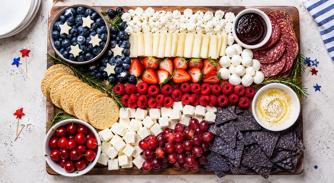 American flag cheese board with fruits meats crackers and dips on wooden platter for party.
