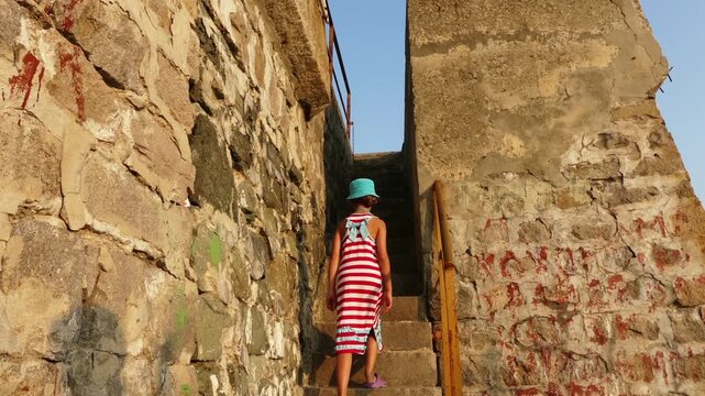 A beautiful girl in a striped dress walks the stairs of a stone lighthouse in the town of Tsarevo on the Black Sea coast in Bulgaria.