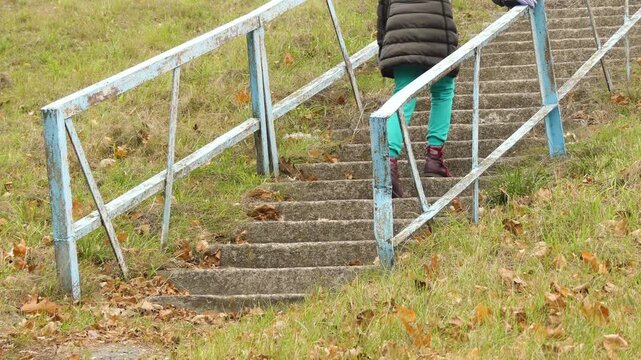 Little girl in autumn jacket walks along steps of old stairs with rusty railing.