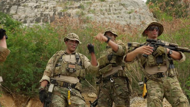 A diverse team of soldiers in full combat gear stacks hands together, demonstrating unity and strategizing for a military operation in a rugged environment.