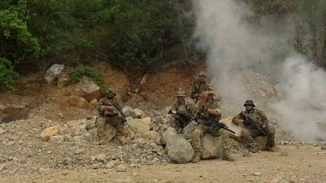 A military special forces team regroups amidst smoke in a rugged, rocky terrain during a tactical operation, showcasing unit cohesion and combat readiness.