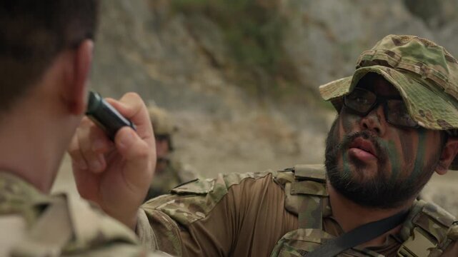 A focused soldier applies camouflage paint to his comrade's face, showcasing teamwork and mission readiness for a tactical operation in the field.