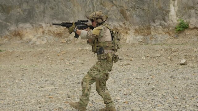 A special forces soldier aims his assault rifle during a tactical training exercise in a rocky, outdoor environment, practicing marksmanship and combat readiness.
