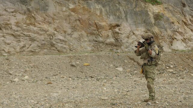 A special forces soldier aims an assault rifle during a tactical training exercise in a rugged quarry, demonstrating combat readiness and marksmanship.