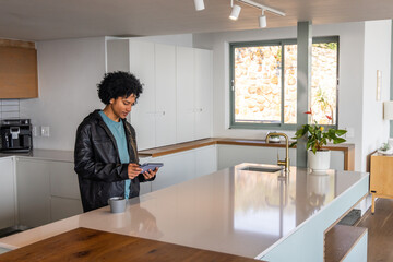 African American man standing at kitchen island checking handheld device near gray mug and plant © wavebreak3