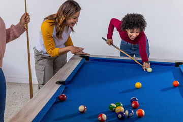Obraz premium Diverse friends playing pool, woman lining shot on pool table with cue, scattered balls, copy space