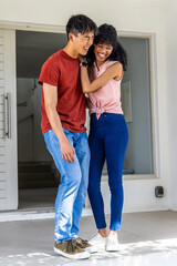 Naklejka premium Diverse couple laughing and leaning after opening door at home entry, celebrating arrival in jeans