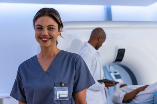 Smiling African American woman in gray scrubs showing badge, colleague using scanner in radiology