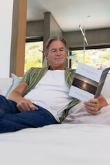 Naklejka premium Mature man reclining on sofa in modern living room reading paperback with sunset cover