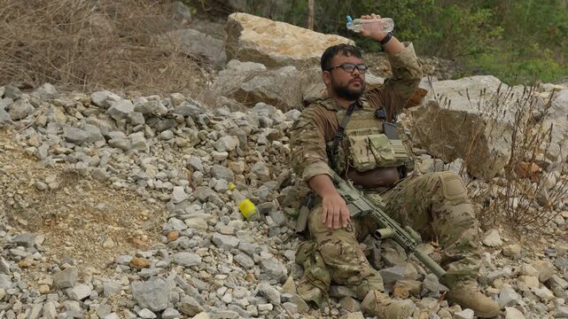 A fatigued special forces operator in tactical gear pours water over his head to cool down, resting during a demanding mission in a rugged, remote location.
