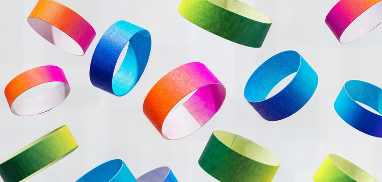 Colorful paper wristbands with rainbow gradient scattered and floating in air symbolizing events festivals and parties for wristband collection.