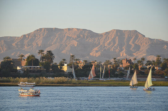 Traditional felucca sailboats and motorboats sailing on the Nile River against the backdrop of the West Bank mountains in Luxor, Egypt during golden hour.