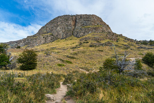 Hiking trail leading to a massive rocky mountain peak in Patagonia, Chile, under a blue sky with clouds