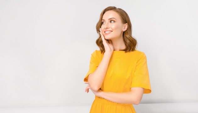 Smiling young woman in yellow dress touching face with hand creative