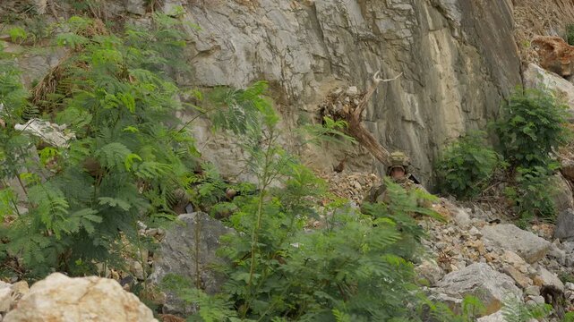 Camouflaged special forces soldiers conduct a covert surveillance mission, securing a tactical position among rugged rocks in a hostile environment.