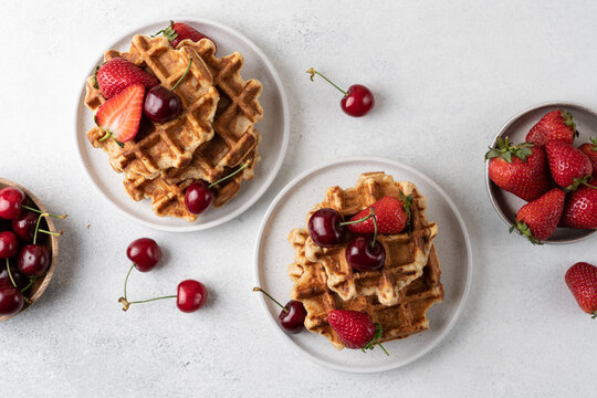 Fresh Belgian cottage cheese waffles served with strawberries and sweet cherries on a light table, top view