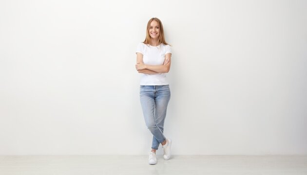 Casual young woman standing with crossed arms smiling indoors against plain white wall