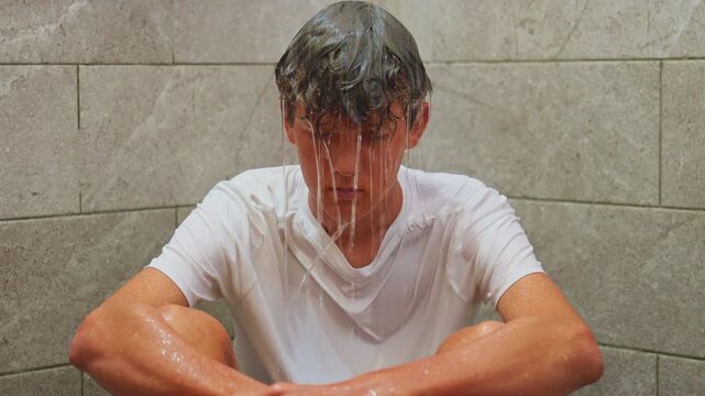 A teenage boy sits in the shower alone water is pouring on him, with his head in his hands, upset and overwhelmed. The kid is feeling upset, emotional, and mentally struggling