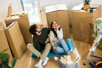 Obraz premium A young couple holding a digital tablet and looking up at the ceiling while imagining a chandelier during relocation