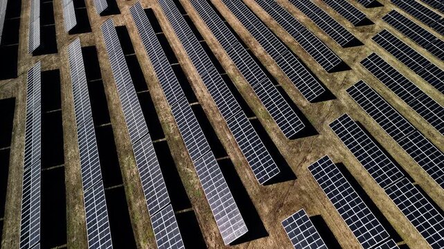 Aerial view of solar panels arranged in rows on a field, showcasing the layout and orientation of photovoltaic cells under bright sunlight in a renewable energy installation