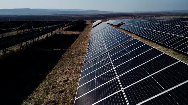 Solar panels arranged in rows capture sunlight on a clear day, showcasing renewable energy technology in a vast field with distant hills under a blue sky