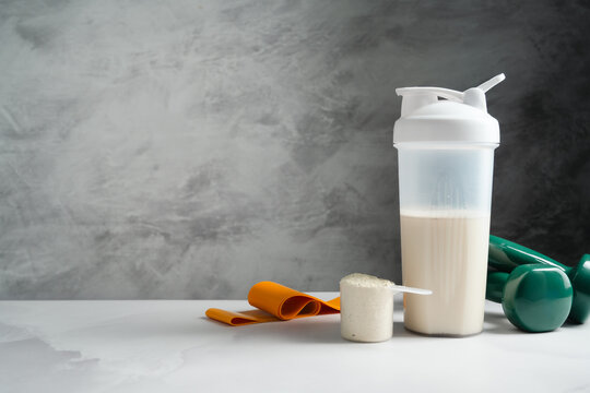 Protein powder and shaker bottle with workout gear on gray background