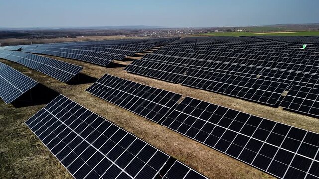 Aerial view of expansive solar panel field with rows of photovoltaic modules arranged in a grid pattern under clear blue sky in a rural landscape
