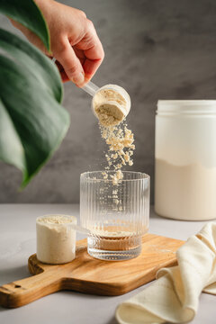 Adding whey protein powder to glass for shake preparation, sports nutrition supplement