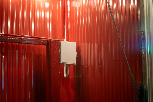 Red corrugated metal wall with electrical box and hose