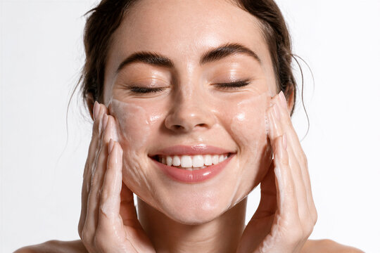 Young woman applying facial cleanser with closed eyes studio