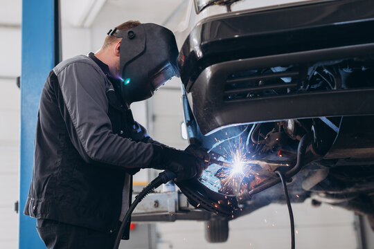 Mechanic welding under car in repair workshop