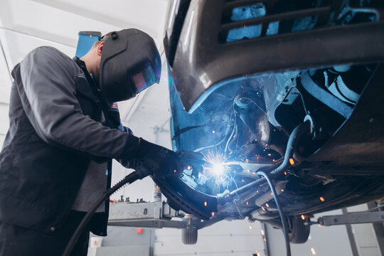 Mechanic welding car undercarriage in repair shop