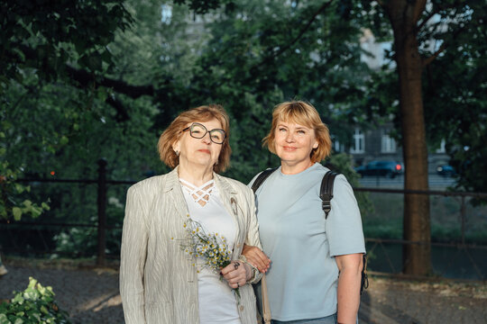 Elegant Senior Women Standing Together Near Riverside Walkway in Modern City District at Sunset