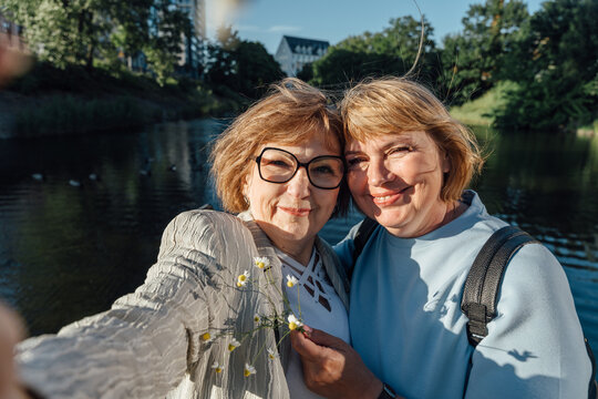 Cheerful Senior Friends Sharing Tender Moment With Chamomile Flowers Near City Waterfront