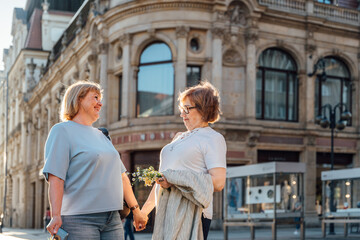 Fototapeta premium Happy Senior Female Friends Holding Hands While Walking Through Historic City Center Together